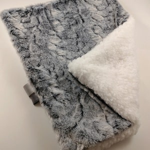 K&ouml;nnte beinhalten: Eine weiche, graue und wei&szlig;e Kunstfell-Decke mit einem flauschigen wei&szlig;en Sherpa-Futter. Die Decke ist in der H&auml;lfte gefaltet und zeigt beide Seiten.