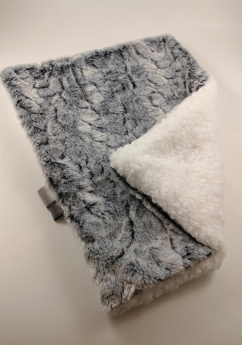 K&ouml;nnte beinhalten: Eine weiche, graue und wei&szlig;e Kunstfell-Decke mit einem flauschigen wei&szlig;en Sherpa-Futter. Die Decke ist in der H&auml;lfte gefaltet und zeigt beide Seiten.
