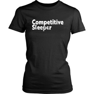 May include: Black t-shirt with the white text "Competitive Sleeper". The shirt has a crew neck and short sleeves. The text has a distressed, textured appearance.