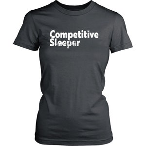 May include: Dark gray t-shirt with the text "Competitive Sleeper" in white, distressed font. The shirt has short sleeves and a crew neck. The text is centered on the front of the shirt.