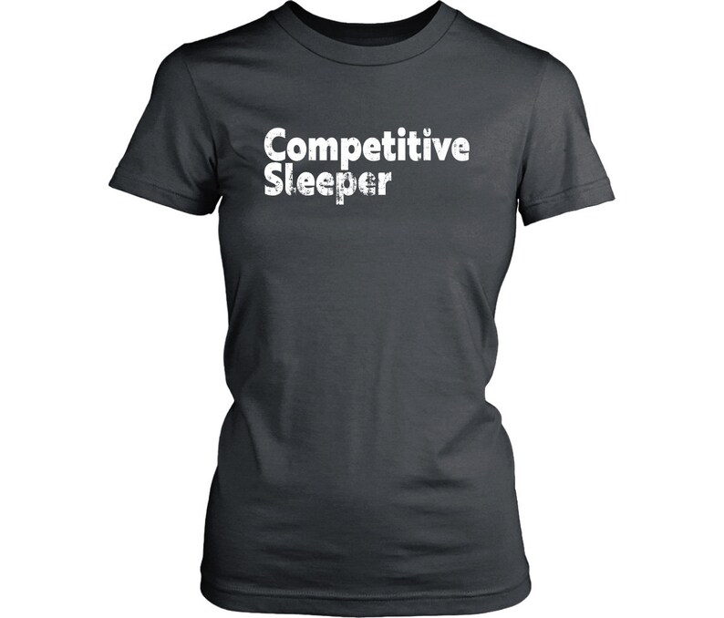 May include: Dark gray t-shirt with the text "Competitive Sleeper" in white, distressed font. The shirt has short sleeves and a crew neck. The text is centered on the front of the shirt.