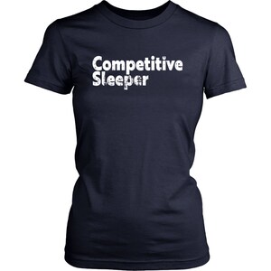 May include: Navy blue t-shirt with the white text "Competitive Sleeper". The shirt has short sleeves and a crew neck. The text has a distressed, slightly textured appearance.