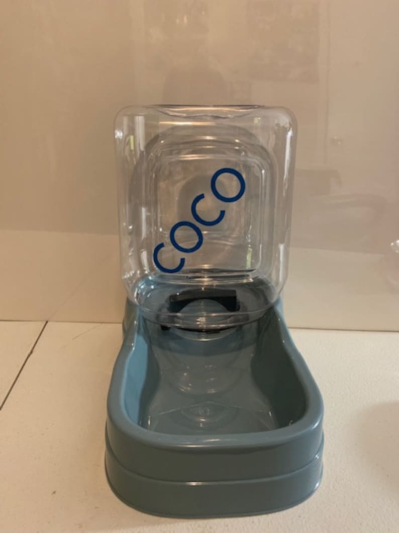 May include: A blue plastic pet water dispenser with a clear plastic reservoir. The reservoir has a label that says "COCO".