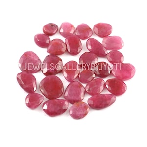 May include: A collection of 20 loose, faceted, pink ruby gemstones. The stones are various sizes and shapes, with a smooth, polished finish.