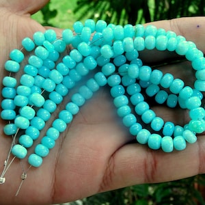 May include: A strand of turquoise blue gemstone beads, strung on silver wire, with a smooth, rounded shape.