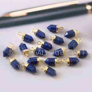 Op de afbeelding: Een verzameling van 15 lapis lazuli edelsteen hangers met een gouden dop. Elke hanger is gevormd als een puntig kristal en heeft een gouden lus om aan sieraden te bevestigen.