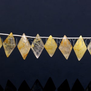 May include: A strand of faceted, clear quartz beads with gold rutilated inclusions. The beads are shaped like diamonds and are strung on a silver wire.