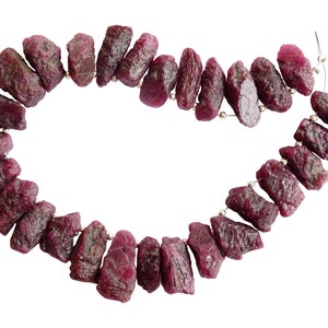 May include: A strand of ruby gemstone beads, each bead is a rough, irregular shape and is strung on a silver wire.