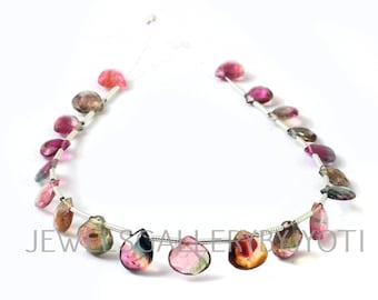 May include: Strands of colorful tourmaline gemstones in shades of pink, green, brown, and black. The teardrop-shaped stones are strung on a thin, silver-colored wire. The image is set against a white background.