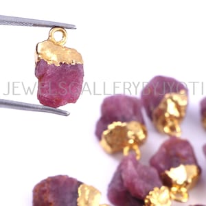 Peut inclure: Un groupe de breloques en rubis rose avec des accents dorés. Les breloques ont la forme de pierres brutes non taillées et ont une boucle dorée pour être attachées à des bijoux.