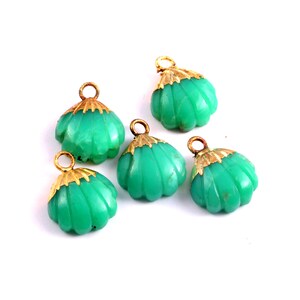 May include: Five green glass shell-shaped charms with gold accents. The charms have a scalloped edge and a loop at the top for hanging.