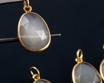 Può includere: Un set di quattro ciondoli in pietra color grigio argento con montature dorate. I ciondoli sono di forma ovale e hanno un design sfaccettato. I ciondoli sono su uno sfondo nero.
