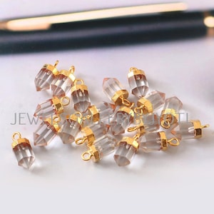 May include: A group of clear quartz crystal pendants with gold-plated jump rings. The pendants are faceted and have a pointed tip. They are perfect for jewelry making.