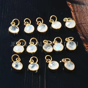 Puede incluir: Una colección de 15 abalorios de piedra lunar chapados en oro, cada uno con un cabujón redondo e iridiscente de piedra lunar. Los abalorios son perfectos para la elaboración de joyas, añadiendo un toque de elegancia y brillo a collares, pulseras y pendientes.
