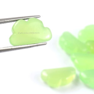 May include: A close-up of a light green cloud-shaped gemstone held by tweezers. The gemstone is smooth and polished. The text "JEWELSGALLERYBYJYOTI" is visible on the gemstone.