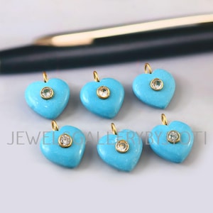 Può includere: Sei ciondoli a forma di cuore turchese con anelli dorati. Ogni ciondolo ha una piccola pietra rotonda e trasparente al centro. Il testo "JEWEL GALLERY BY JOTI" è visibile nella parte inferiore dell'immagine.