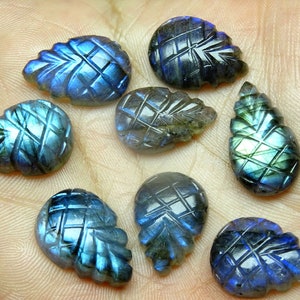 May include: Eight carved labradorite gemstone cabochons in a teardrop shape with a pineapple design. The stones are iridescent with blue, green, and black hues.