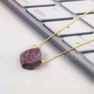 Puede incluir: Un collar de cadena dorada con un colgante de rubí rosa en bruto. El rubí es una piedra natural en bruto de color rosa intenso.