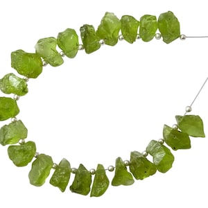 May include: A strand of raw, green peridot beads strung on a silver wire. The beads are irregular in shape and size, and have a natural, rough texture.