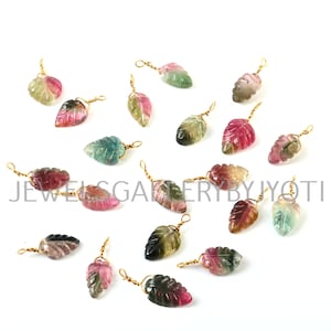 May include: A collection of 16 multi-colored gemstone leaf charms with gold-toned wire loops. The leaves are carved from watermelon tourmaline and have a variety of colors, including pink, green, and black.