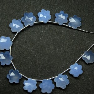 Puede incluir: Una hebra de cuentas de piedras preciosas de color azul claro, cada cuenta tiene forma de flor con cinco pétalos. Las cuentas están enhebradas en un alambre de plata.