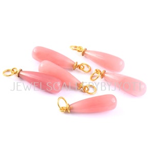 May include: Six pink teardrop-shaped gemstone pendants with gold-toned metal loops. The pendants are arranged in a semi-circle on a white background.