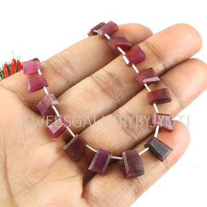 May include: A strand of red gemstone beads, likely rubies, with a rectangular shape. The beads are strung on silver wire.