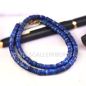 May include: A necklace composed of small, faceted, deep blue lapis lazuli disc beads arranged in a circular pattern. The necklace features a gold-toned metal lobster claw clasp and is overlaid with the white text JEWELSGALLERYBYJYOTI.
