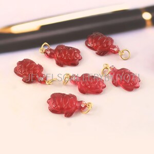 May include: Six small, translucent red turtle-shaped charms with carved shell details. Each turtle features a gold-toned metal jump ring attached to its head. The charms are arranged in a cluster, and the text JEWELGALLERYBYJYOTI is visible.