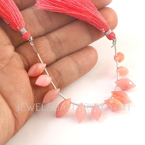 Könnte beinhalten: Eine Kette aus rosa Edelsteinperlen mit einer Quaste an jedem Ende. Die Perlen sind hellrosa und auf einem silbernen Draht aufgereiht. Die Quasten sind leuchtend korallenfarben.