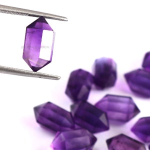 May include: A group of purple amethyst crystal points, some are held in tweezers. The points are faceted and have a pointed tip. The crystals are on a white background.