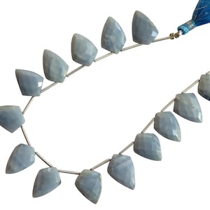 Puede incluir: Una hebra de cuentas de piedras preciosas de color azul claro con forma de lágrima facetada. Las cuentas están enhebradas en un alambre de plata y tienen un borla azul en un extremo.