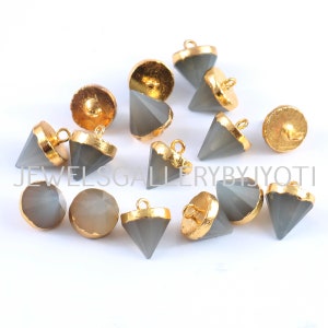Könnte beinhalten: Eine Sammlung grauer, pyramidenförmiger Knöpfe aus Edelstein mit goldenen Akzenten. Die Knöpfe haben eine Schlaufe oben zum Anbringen an Kleidung oder anderen Gegenständen.
