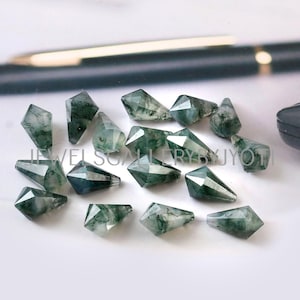 May include: A collection of 15 green moss agate gemstone pendants in a teardrop shape. The pendants are faceted and have a natural, organic look.