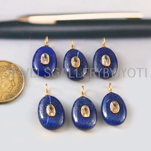May include: Six oval-shaped, deep blue pendants with gold-colored bails. Each pendant features a central, light-colored, oval-shaped stone. The pendants are arranged on a light-colored surface, with a gold coin visible on the left.