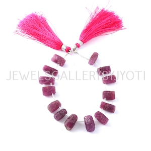 Könnte beinhalten: Eine Kette aus rosafarbenen Rubin-Edelsteinen mit einem silbernen Draht, der durch jede Perle gezogen ist. Die Perlen sind rechteckig und haben eine raue, natürliche Oberfläche. Die Kette ist mit zwei rosafarbenen Quasten verziert.
