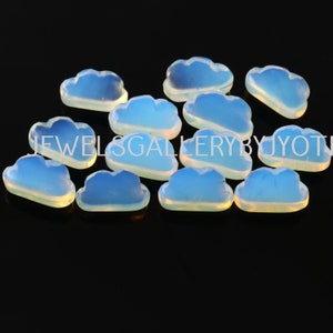May include: A collection of cloud-shaped opalite gemstones. The opalite stones are a light blue color with a translucent quality. The text "JEWELS GALLERY BY JYOTI" is visible in the image. The gemstones are arranged on a black surface.