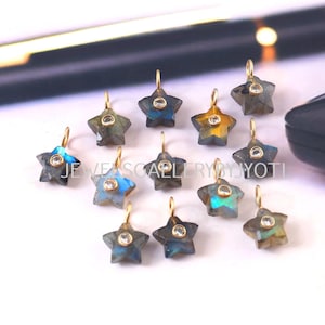 May include: A collection of star-shaped gemstone pendants with gold-colored loops. The pendants are a mix of blue, gray, and yellow hues, with a small, clear stone set in the center of each star. The text "JEWELSCALLERYBYJYOTI" is visible.