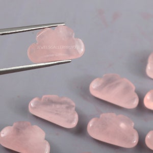 Könnte beinhalten: Sechs rosa Rosenquarzsteine, die in Wolkenform geschnitzt sind. Die Steine sind glatt und poliert. Der Text "JEWELSGALLERYBYJYOTI" ist auf einem der Steine sichtbar.