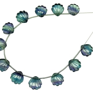 Op de afbeelding: Een streng blauwe en groene fluorite edelsteen kralen, gesneden in de vorm van schelpen, geregen op een zilveren draad.