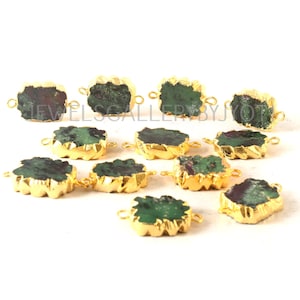 May include: A collection of raw ruby and emerald gemstone connectors with gold-plated edges. The gemstones have a rough, natural texture, with a mix of deep red and green hues. Each connector has small loops for attaching to jewelry.