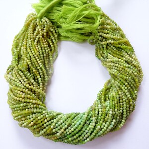May include: A strand of green gemstone beads, likely chrysoprase, with a faceted finish. The beads are small and uniform in size, and the strand is long and full.