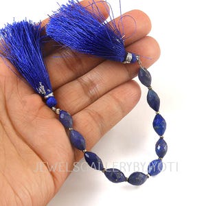 Könnte beinhalten: Eine Kette aus tiefblauen Lapislazuli-Perlen mit zwei passenden blauen Quasten-Akzenten. Die oval geformten Perlen sind mit silberfarbenen Elementen aufgefädelt. Der Text "JEWELSCALLERYBYJYOTI" ist sichtbar.
