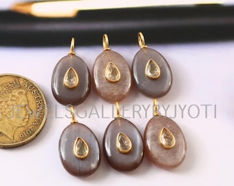 Può includere: Sei pendenti ovali con una pietra a forma di goccia di colore chiaro incastonata in un metallo color oro. I pendenti sono un mix di tonalità grigie e marroni. I pendenti sono esposti con una moneta d'oro.