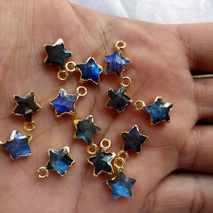 May include: A collection of 12 gold-plated star-shaped pendants featuring blue labradorite gemstones. The pendants have a loop at the top for attaching to jewellery.