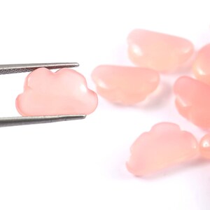 May include: Several small, pale pink cloud-shaped beads. One is held by tweezers, with others scattered on a white background. The beads have a smooth, glossy finish and are ideal for jewellery making.