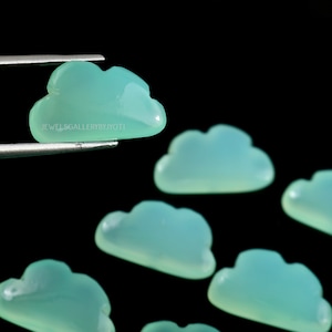 May include: A group of seven light green gemstone cloud shaped cabochons. The cabochons are smooth and polished. The cabochons are arranged in a semi-circle.