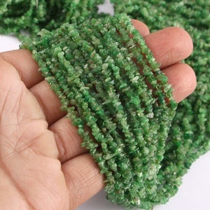 May include: A strand of green gemstone chip beads. The beads are small and irregular in shape, and they are strung on a clear thread. The beads are a vibrant green color, and they have a slightly translucent appearance.