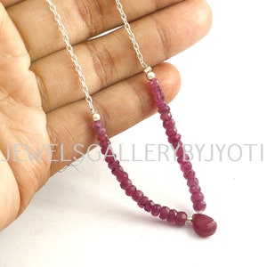 Op de afbeelding: Een zilveren ketting met een roze robijn hanger en roze robijn kralen. De ketting ligt op een hand.