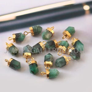 Könnte beinhalten: Eine Sammlung von grünen Edelstein-Anhängern mit goldfarbenen Akzenten. Die Anhänger sind in Form eines spitz zulaufenden, länglichen Sechsecks geformt.